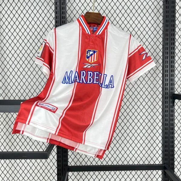 Camiseta local Atlético de Madrid 1999-2000 con franjas rojas y blancas, cuello tipo polo, escudo bordado y patrocinio de Marbella