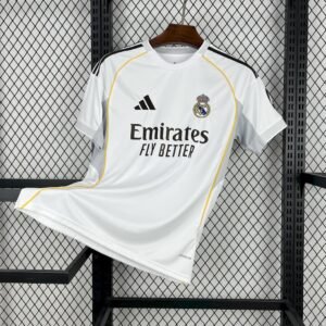 Camiseta local Real Madrid 2025‑26 blanca con detalles en amarillo, gris claro y logotipos en negro, inspirada en el estadio Santiago Bernabéu
