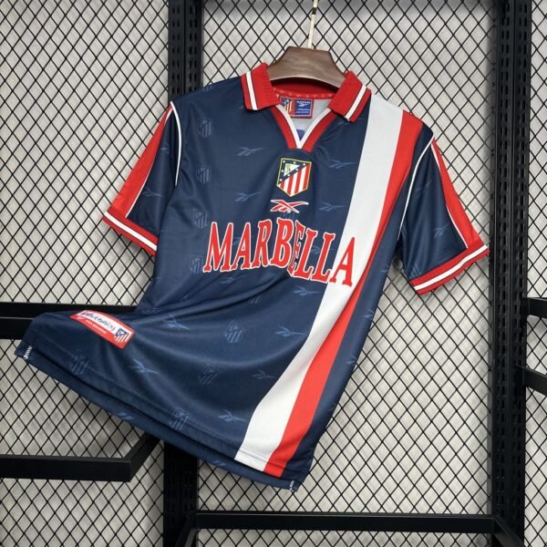 Camiseta visitante Atlético de Madrid 1998-99 en azul marino con franja roja y blanca, escudo bordado y patrocinio Marbella