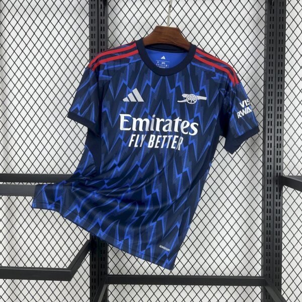 Camiseta visitante Arsenal 25/26 azul marino con rayos azul real, detalles rojos y logos en plata metálica