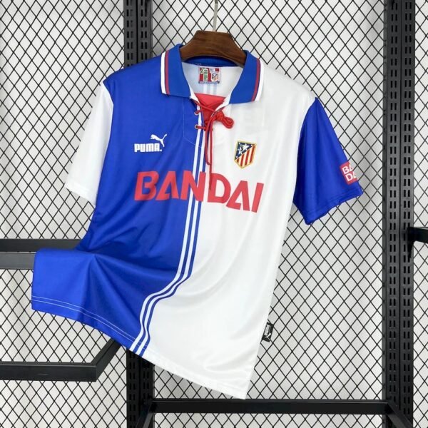 Camiseta tercera Atlético de Madrid 1996-97 con diseño dividido en blanco y azul, escudo bordado, logo Puma y patrocinio Bandai